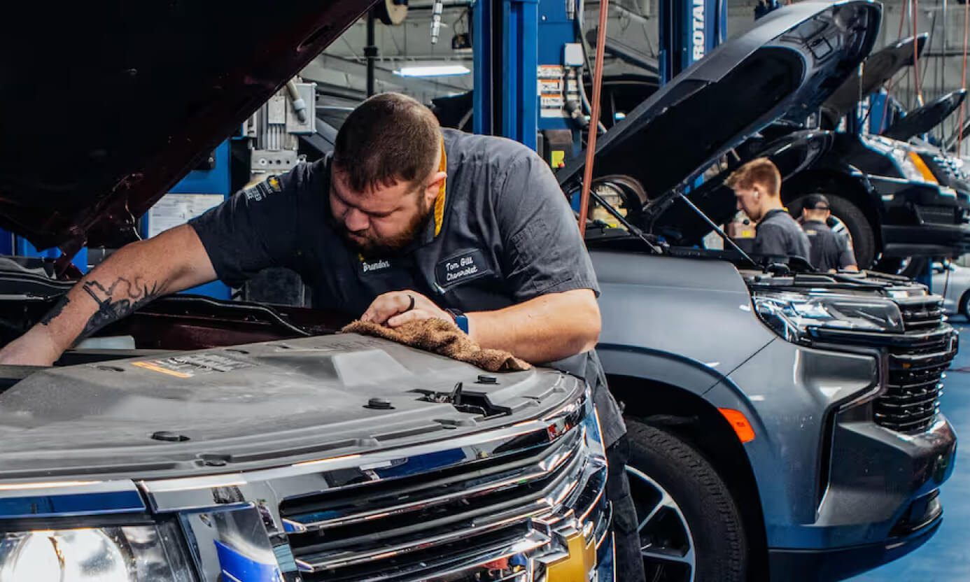 Chevrolet mechanic repairing a vehicle engine inside a busy dealership service department.
